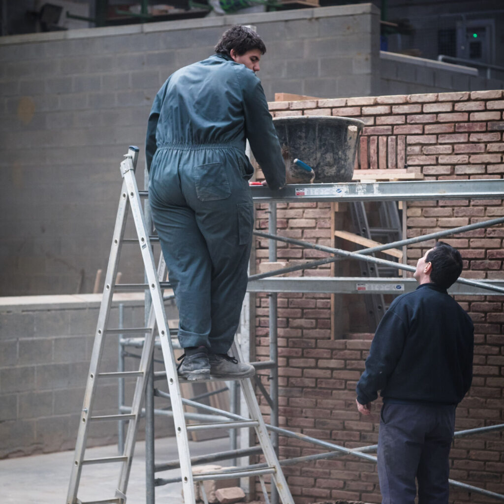 leerling op ladder en leerling naast stelling bekijken een zelfgebouwd muurtje