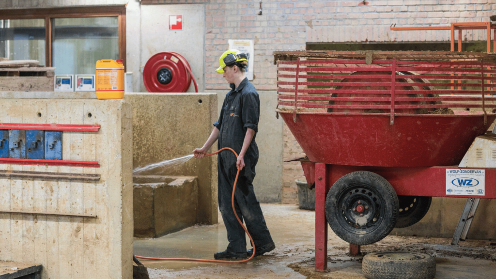 leerling met helm en werkpak en waterslang in de hand