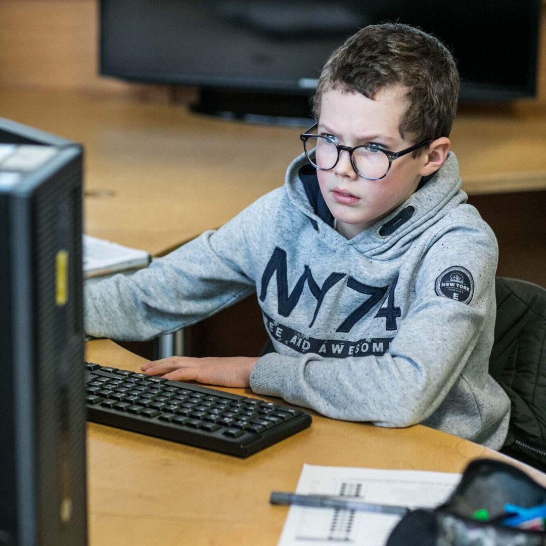 een jongen met bril doet taken op de computer