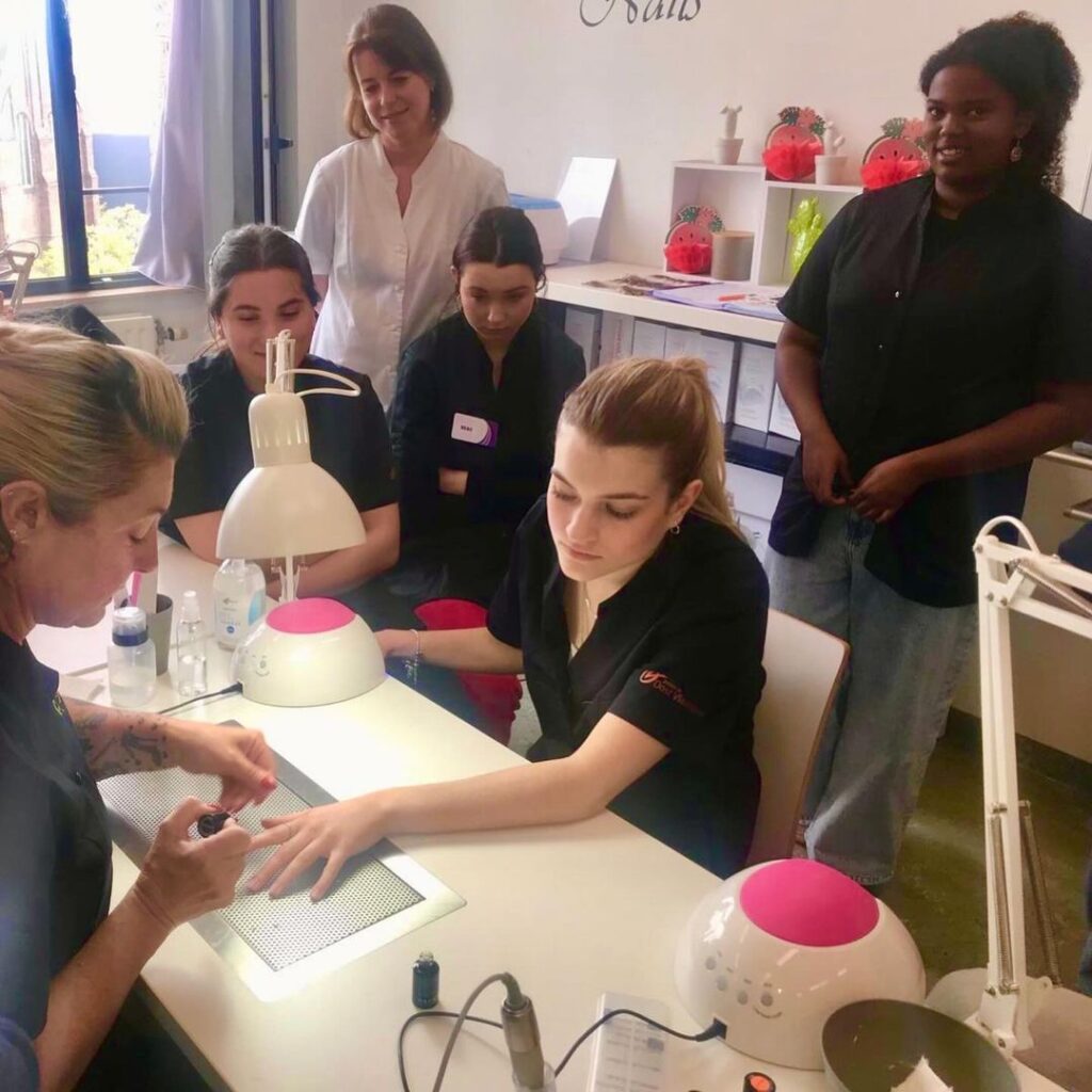 de nagels van een leerling worden gelakt tijdens een demo op school, enkele leerlingen kijken toe