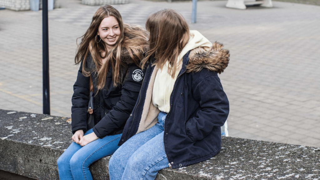 twee leerlingen zitten op een muurtje op de speelplaats