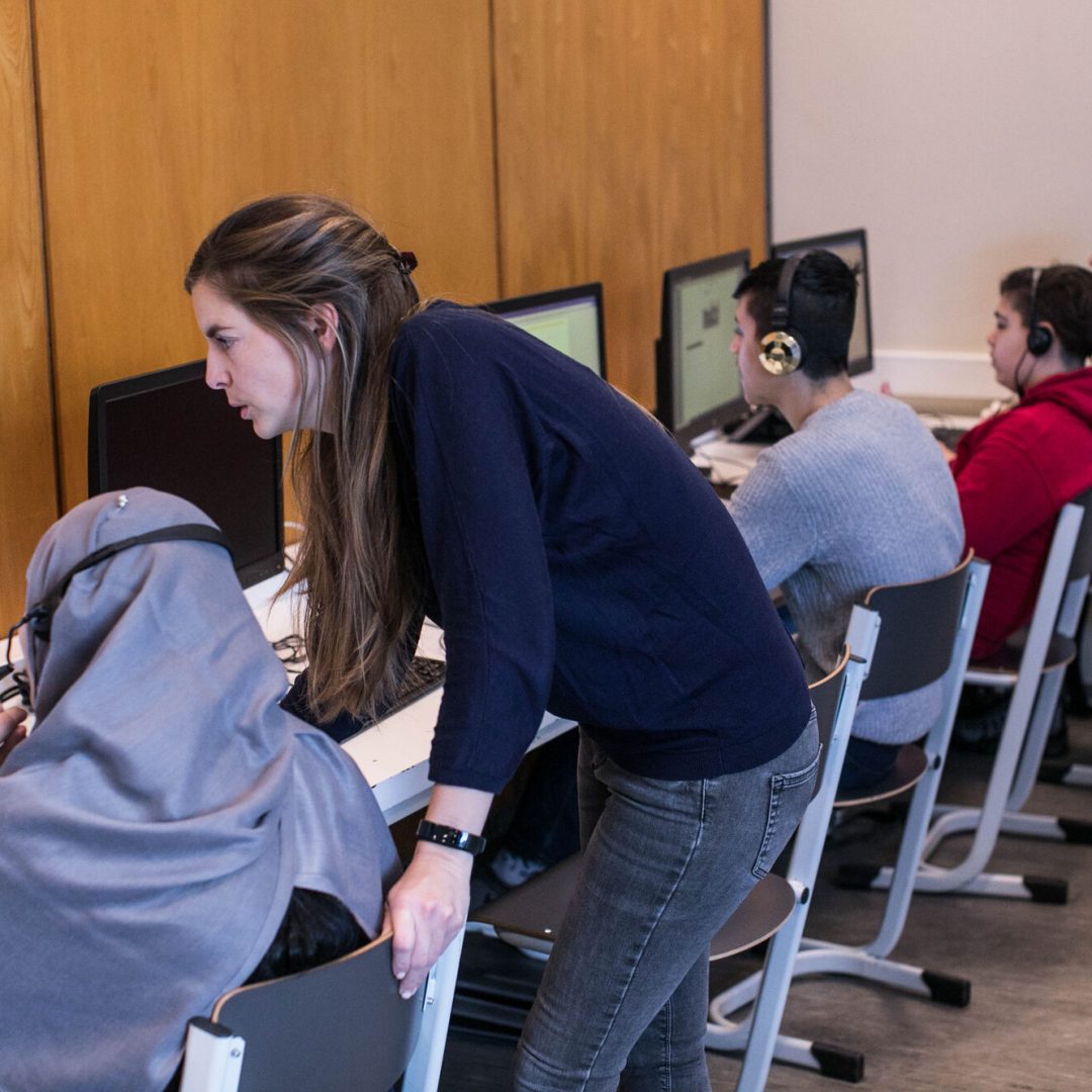 leerkracht helpt enkele leerlingen met oefeningen op de computer