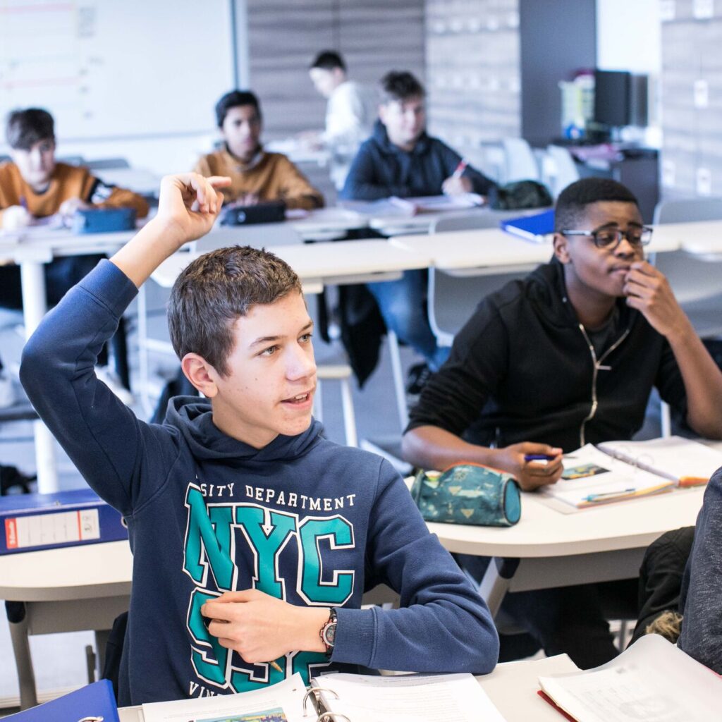 leerling zit in de klas en steekt zijn hand op