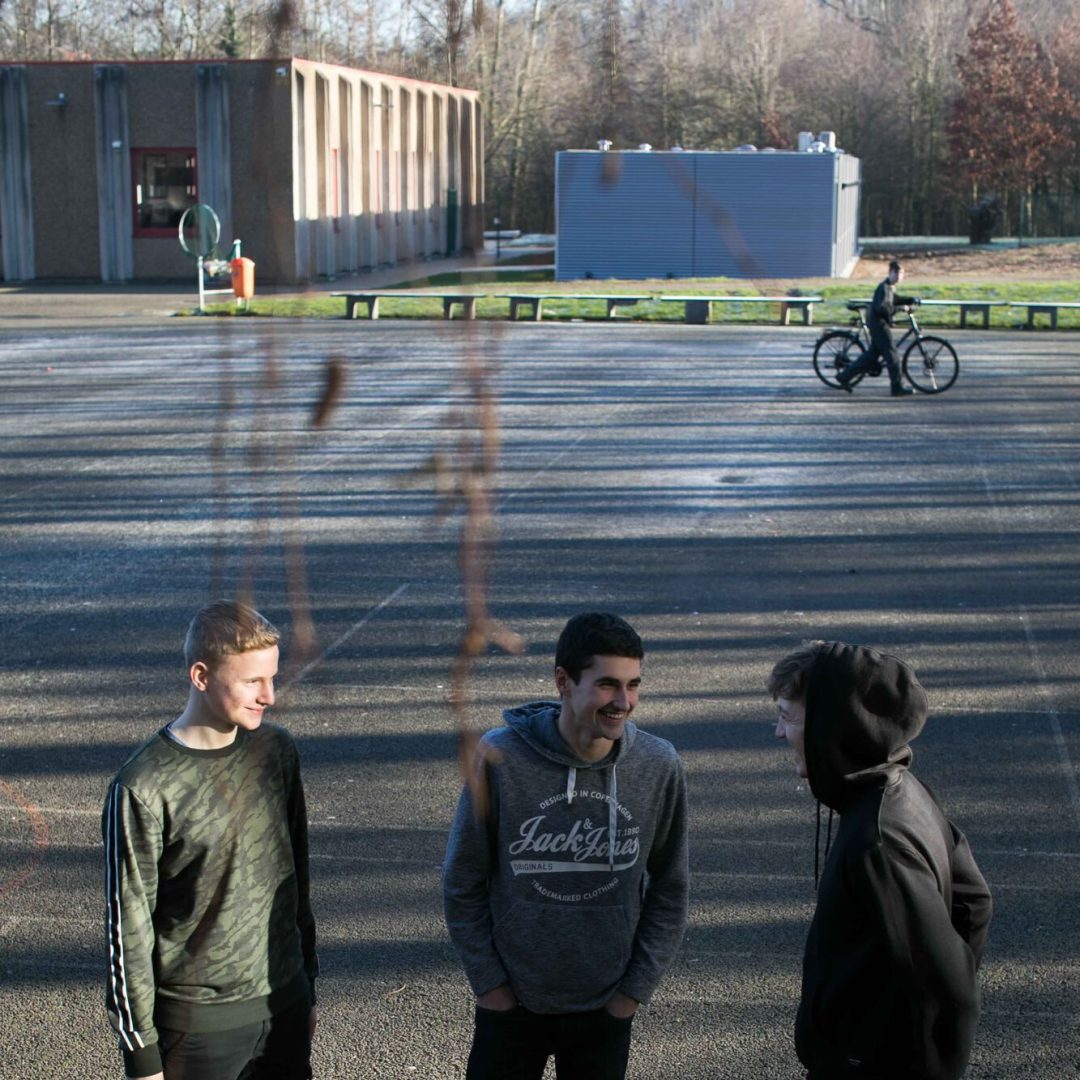 drie leerlingen op de speelplaats met fietser in de achtergrond